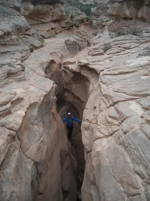 Person in the bottom of a slot canyon, looking up at the camera, with a wider, taller canyon above.