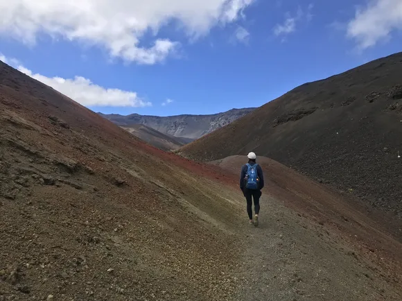 A hiker walks a trail between two red and yellow cinder cones.